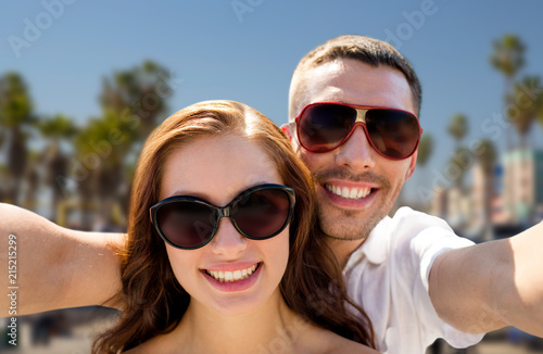 travel, tourism and people concept - smiling couple wearing sunglasses making selfie over venice beach background in california
