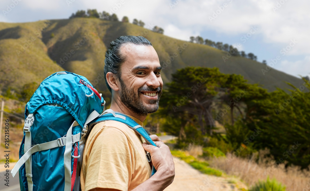 adventure, travel, tourism, hike and people concept - close up of smiling young man with backpack over big sur hills of california background