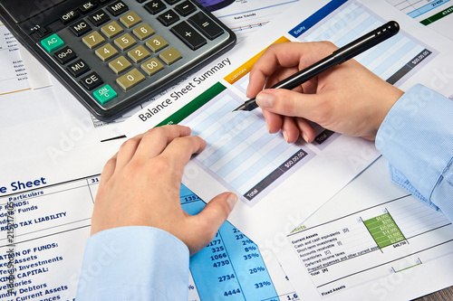 human hands write balance sheet summary on a background balances sheets with calculator