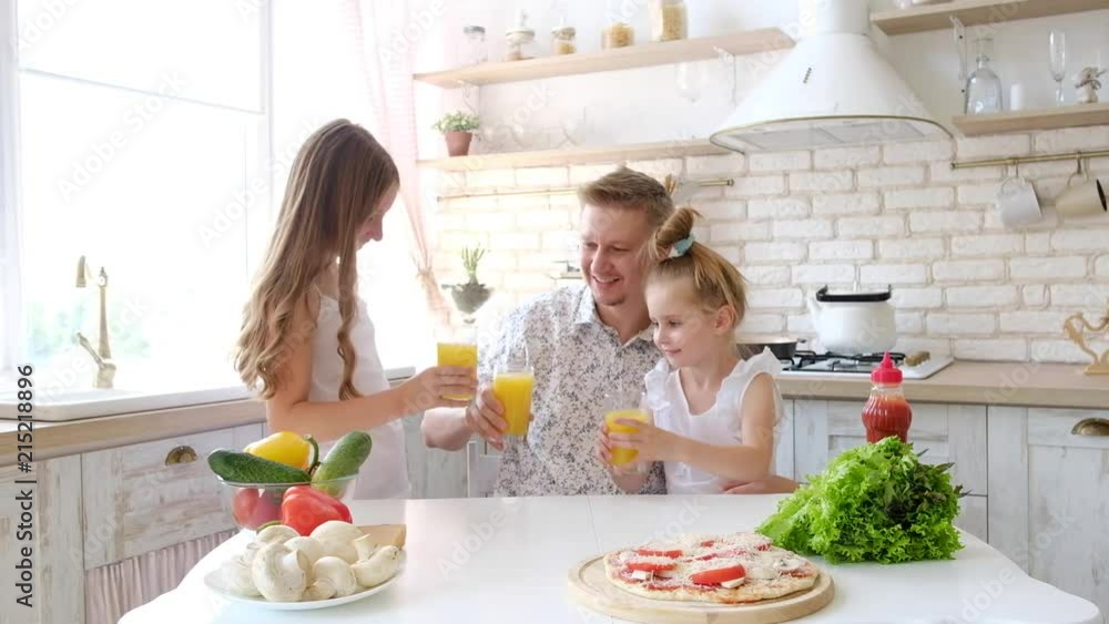 Father and daughters drinking orange juice in the kitchen and making pizza Father and daughters drinking orange juice in the kitchen and making pizza
