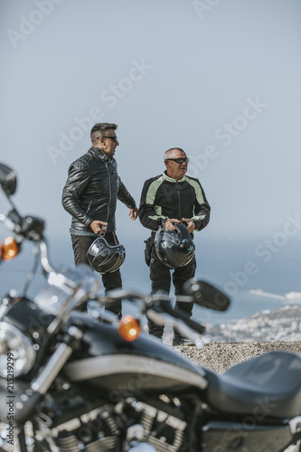 Two men having a break after motorbike ride, with the sea and blue sky in the background.