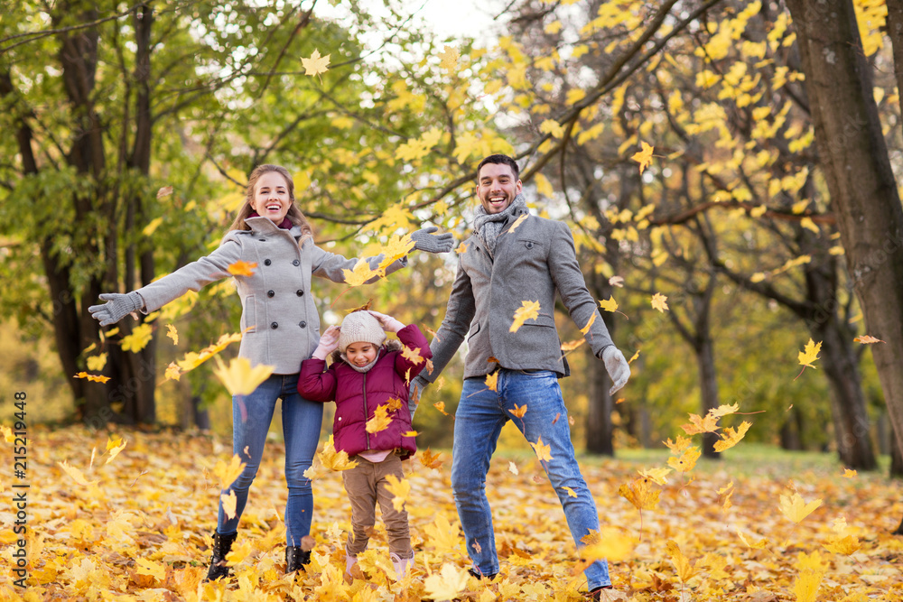 family, season and people concept - happy mother, father and little daughter playing with autumn leaves at park
