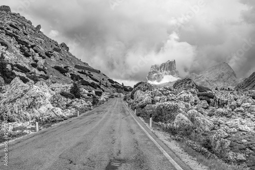 Empty deserted road in black and white leading to menacing stormy, cloudy mountains in the Dolomites, Italy