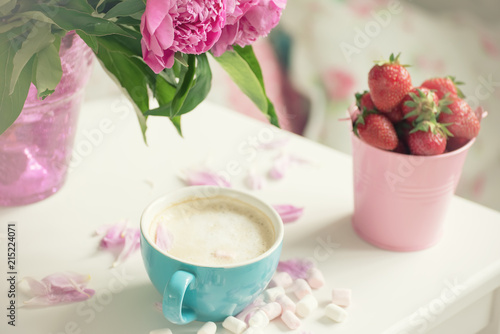 Gentle flowers are pink peonies, coffee with fluffy white milk foam and strawberries. The atmosphere of romance and pleasure. 