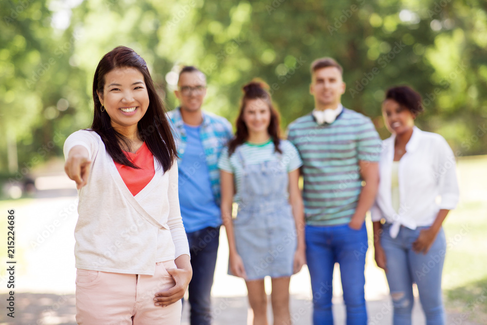 people, friendship and international concept - happy smiling asian woman pointing at you and group of happy friends outdoors people, friendship and international concept - happy smiling asian woman pointing at you and group of happy friends outdoors