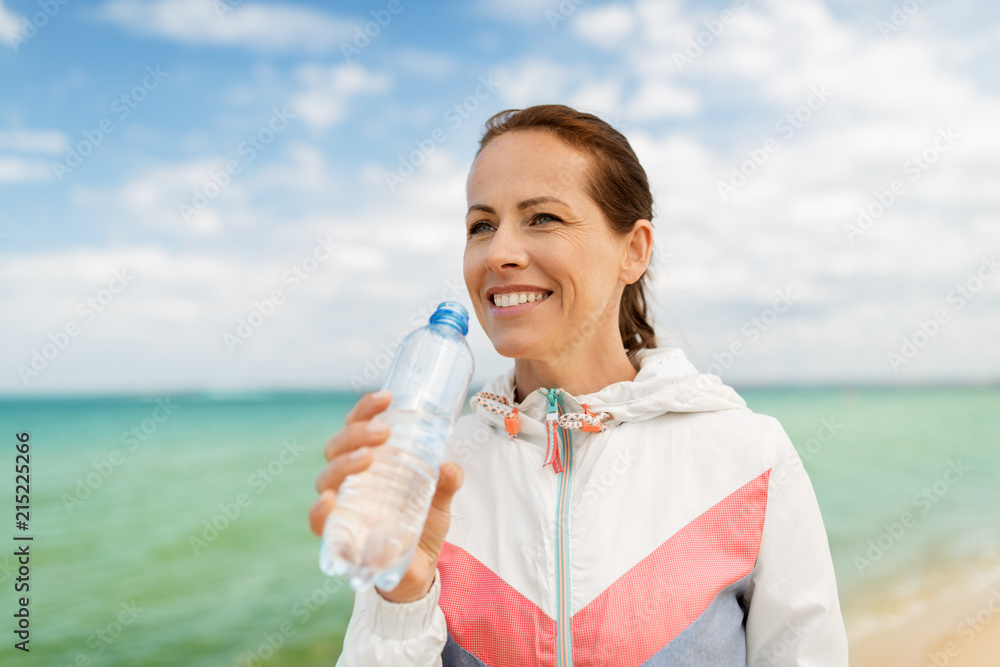 fitness, sport and healthy lifestyle concept - woman drinking water after exercising on beach fitness, sport and healthy lifestyle concept - woman drinking water after exercising on beach