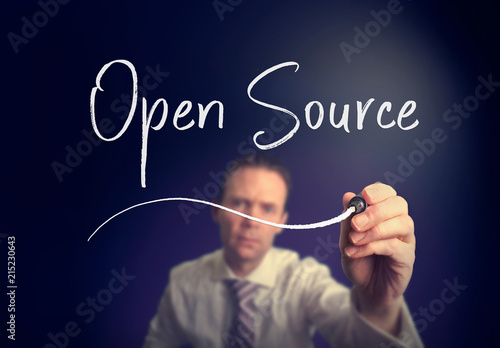 A businessman writing a open source concept with a white pen on a clear screen.