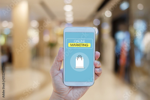 Hand holding smartphone with text ONLINE MARKETING on screen over blurred in shopping mall background