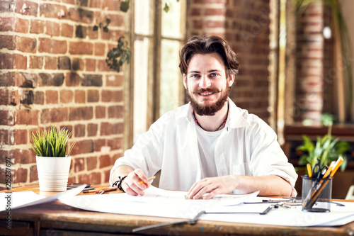 Young ambitious bearded architect in white shirt drawing a blueprint of new contemporary house in loft office