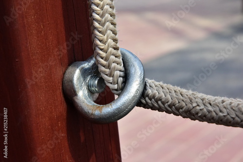 Stailess steel anchor loop. Detail of fixing the white nylon rope to the wooden beam on the structures of the children's playground photo