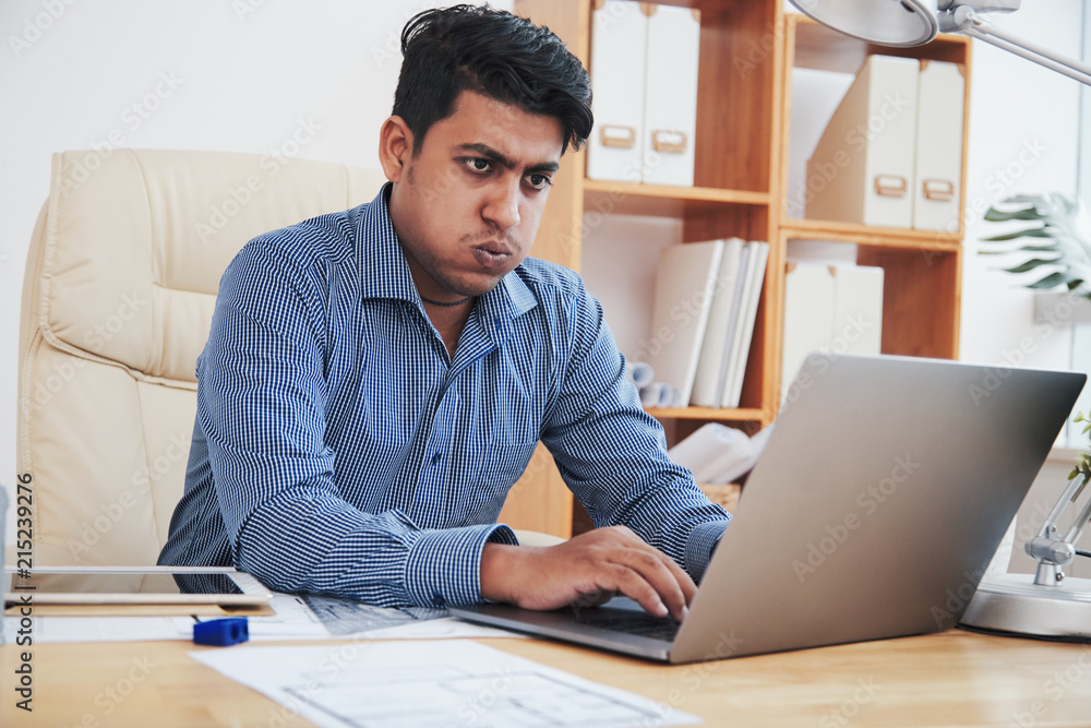 Tired Indian businessman typing on laptop and working in office Tired Indian businessman typing on laptop and working in office