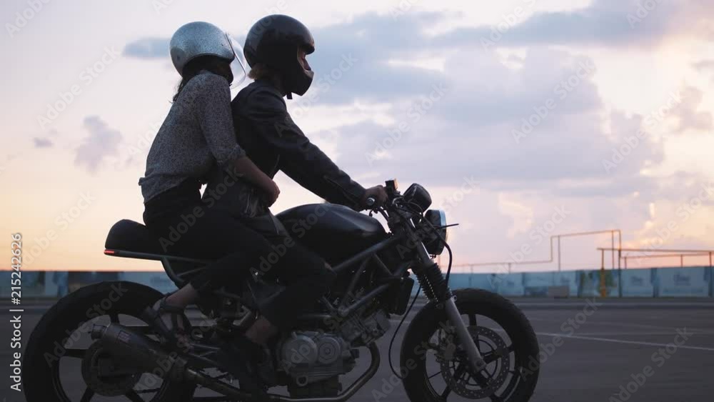 Young couple in helmets riding on motorcycle in city with beautiful sunset sky background, slow motion Young couple in helmets riding on motorcycle in city with beautiful sunset sky background, slow motion