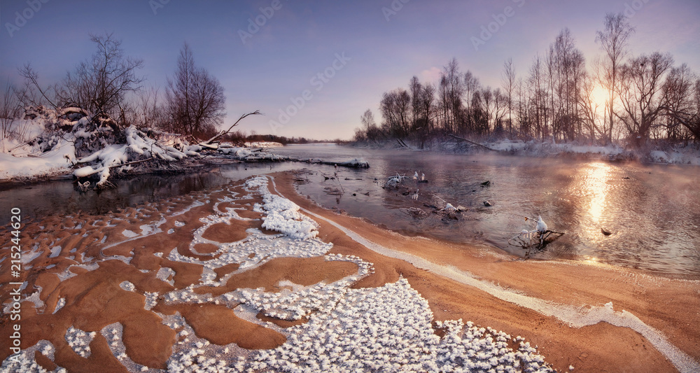 A Beautiful Winter Morning Landscape: The Sun Rising Over The Forest And The Sandy Shallows Of The River, Covered With Frost Crystals. Belarusian Winter Panoramic Landscape With Sun, River And Forest