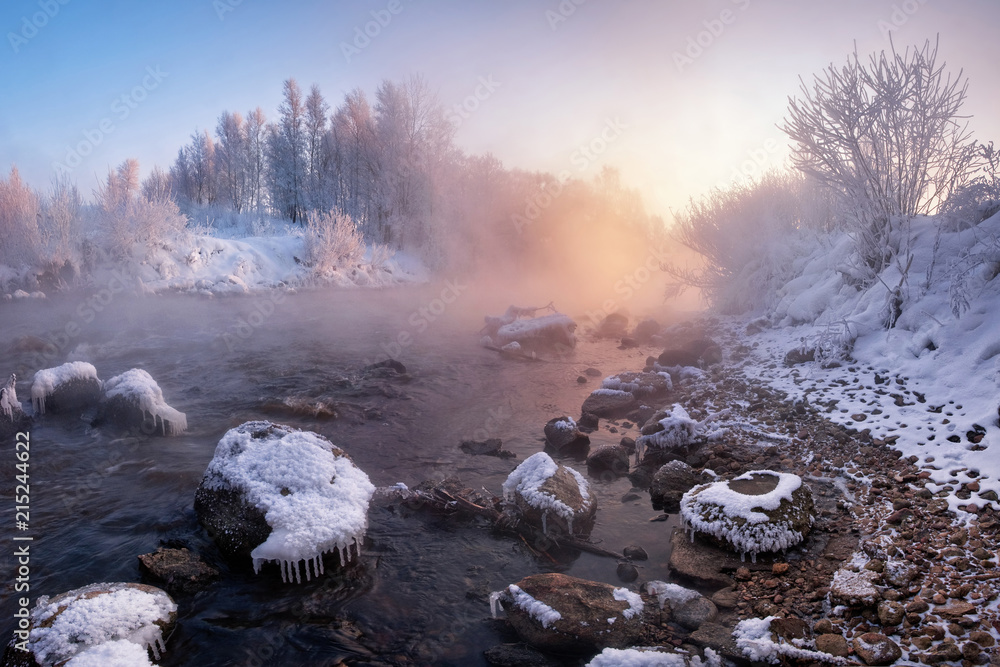 Winter Landscape: The River Flowing Among The Snow-Covered And Ice-Covered Stones And The Rose Sun Rising Over The Forest. Pinky Winter Morning In Belarus.Morning Landscape With WInter Rocky River
