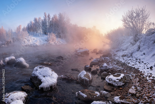 Obraz na płótnie Winter Landscape: The River Flowing Among The Snow-Covered And Ice-Covered Stones And The Rose Sun Rising Over The Forest. Pinky Winter Morning In Belarus.Morning Landscape With WInter Rocky River w salonie