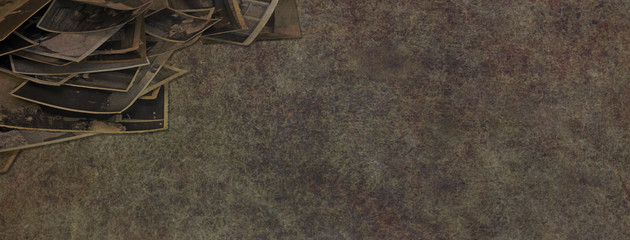 Rustic old photographs background banner- random pile of untidy sepia photographs in left corner with copy space on rustic grunge dark coloured background
