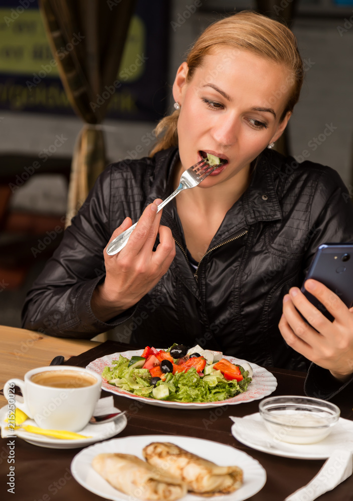businesswoman eating salad in an outdoor cafe. Healthy lifestyle: girl eating green tasty food and checks email on your phone