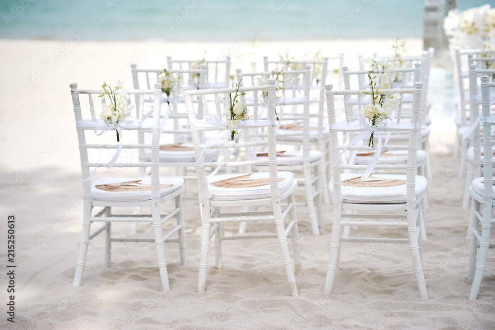 Back side of white chiavari chairs, wedding chairs settings for beach wedding venue on the white sand with ribbin of rose flower petals decoration