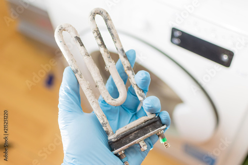 Washing machine repair. Hand of repairer with turbular electric heating element photo