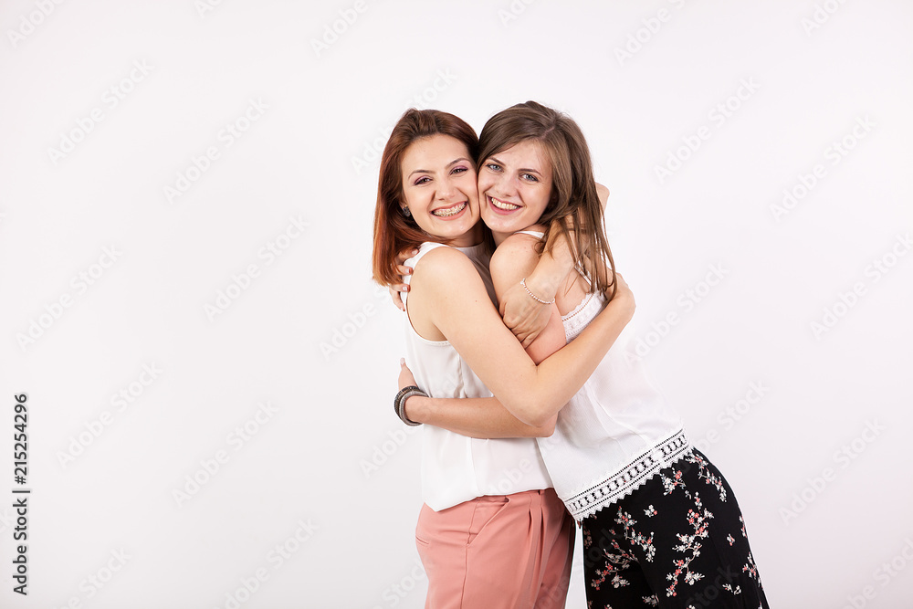 Two beautiful girl friends embracing each other on white wall in studio photo Two beautiful girl friends embracing each other on white wall in studio photo