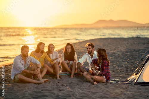 Young friends with guitar at beach. friends relaxing on sand at beach with guitar and singing. © luckybusiness