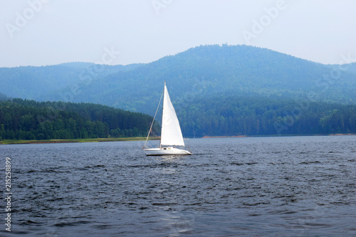 White yacht. Sailboat. Boat goes by sea. Motor ship.Pier. Port. Island in the sea. Mountains. Rocky shore. Beach. Sea blue water. Waves. Sea. Seascape. Rocky.