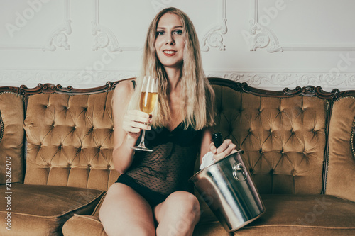 Beautiful adult lady with a gorgeous ass sitting on the royal couch. Model is dressed in fashionable lingerie. Girl with a glass of champagne shows her flirting mood. Concept of sexual fantasies