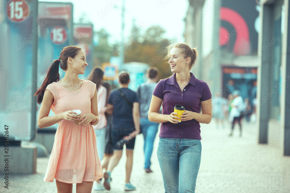 Beautiful girls holding paper coffee cup and enjoying the walk in the city Beautiful girls holding paper coffee cup and enjoying the walk in the city