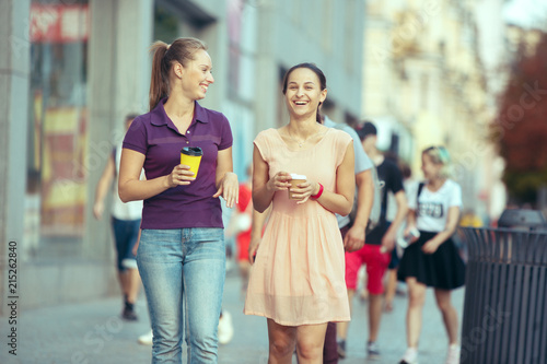 Beautiful girls holding paper coffee cup and enjoying the walk in the city