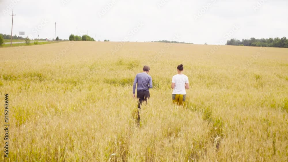 Dolly shot. Two scientists environmentalists walking through the wheat field. Rear view. Then they stoping. Woman looking in the papers, man making notes in a diary Dolly shot. Two scientists environmentalists walking through the wheat field. Rear view. Then they stoping. Woman looking in the papers, man making notes in a diary