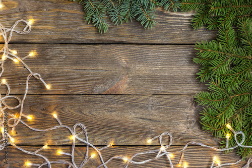 Christmas close-up of Christmas tree branches and Chistmas lights on vintage wooden background. Top view of a Christmas workplace. New Year frame or Xmas Mockup.