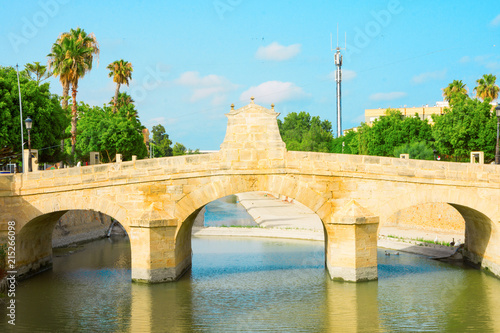 Charles III bridge over the Segura river in Rojales in Alicante province Spain. Summer sunny day blue sky green trees reflections in water. Beautiful panorama with no people. High resolution poster photo