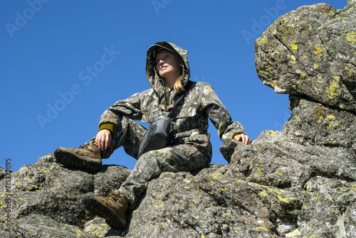 smiling hiker girl looking into the distance, sitting on top of a cliff photo