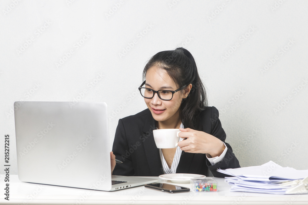 Happy business Asian woman working with laptop at white working table, diligent professional working woman drinking coffee while working on laptop computer. Happy business Asian woman working with laptop at white working table, diligent professional working woman drinking coffee while working on laptop computer.