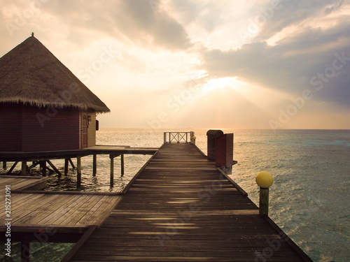 Fototapeta Naklejka Na Ścianę i Meble -  Perspective view of wooden pier and bungalow over the sea in sunset time at Maldives island for summer vacations holiday concept.