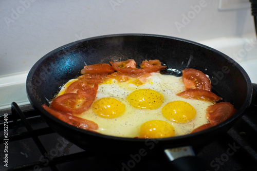 Fried eggs with tomato in a frying pan. Scrambled eggs and tomato on frying pan