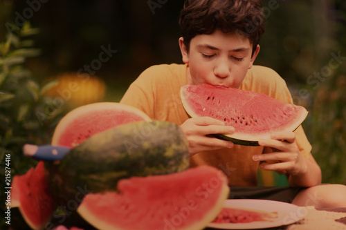 teenager boy with cut water melon close up photo on green garden background photo