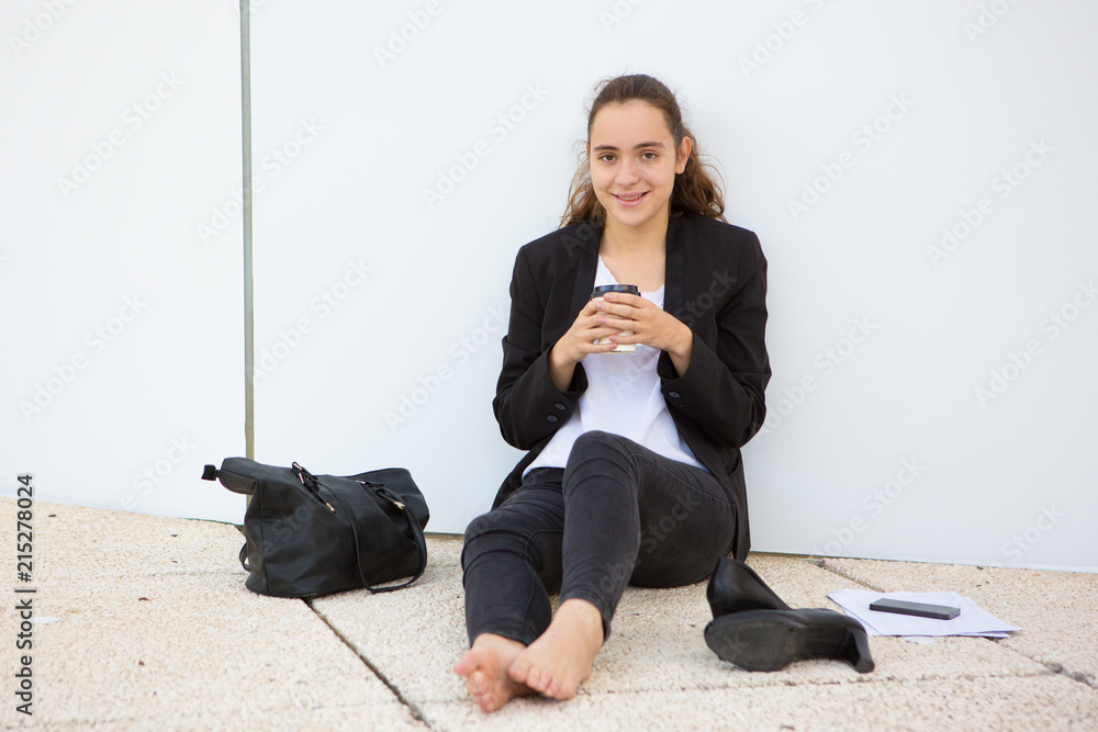 Cheerful young female employee fed up with office dress code. Positive  barefoot girl in jacket sitting on ground near her shoes and drinking  takeaway coffee. Coffee break and burnout concept Photos |