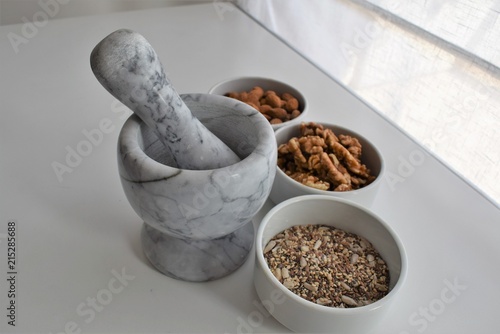 Three white containers with almonds, walnuts and a mixture of sunflower, sesame and chia seeds near a marble mortar.