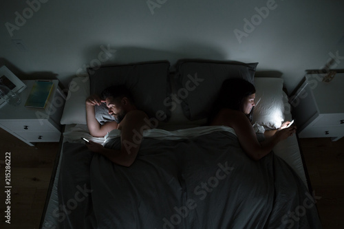 Couple using their phones in bed at night