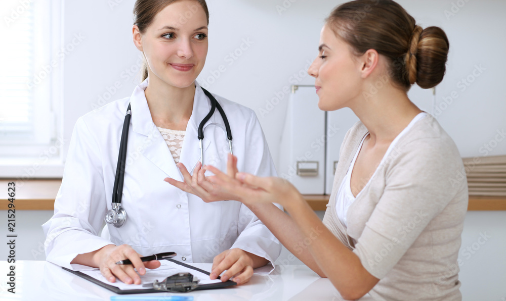 Doctor and patient having a pleasure talk while sitting at the desk at hospital office. Healthcare and medicine concept Doctor and patient having a pleasure talk while sitting at the desk at hospital office. Healthcare and medicine concept