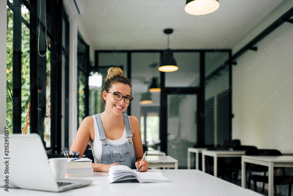 © bnenin - Portrait of a smiling millenial girl studying in modern study room. © bnenin - Portrait of a smiling millenial girl studying in modern study room.