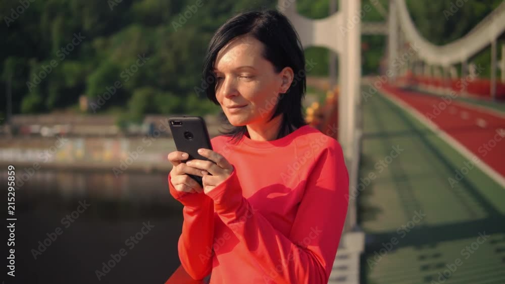 lady typing a message while doing her morning jog. she is training at the bridge. lady typing a message while doing her morning jog. she is training at the bridge.