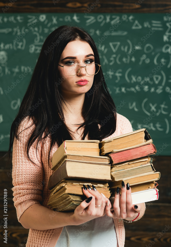 She loves reading. Girl bookworm take books in library. Student excellent  fond of reading. Diligent student preparing for exam test. Girl nerd holds  heavy pile of old books, chalkboard background Stock Photo