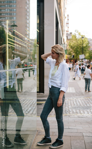 Young blonde woman looking at her reflection in a glass wall photo