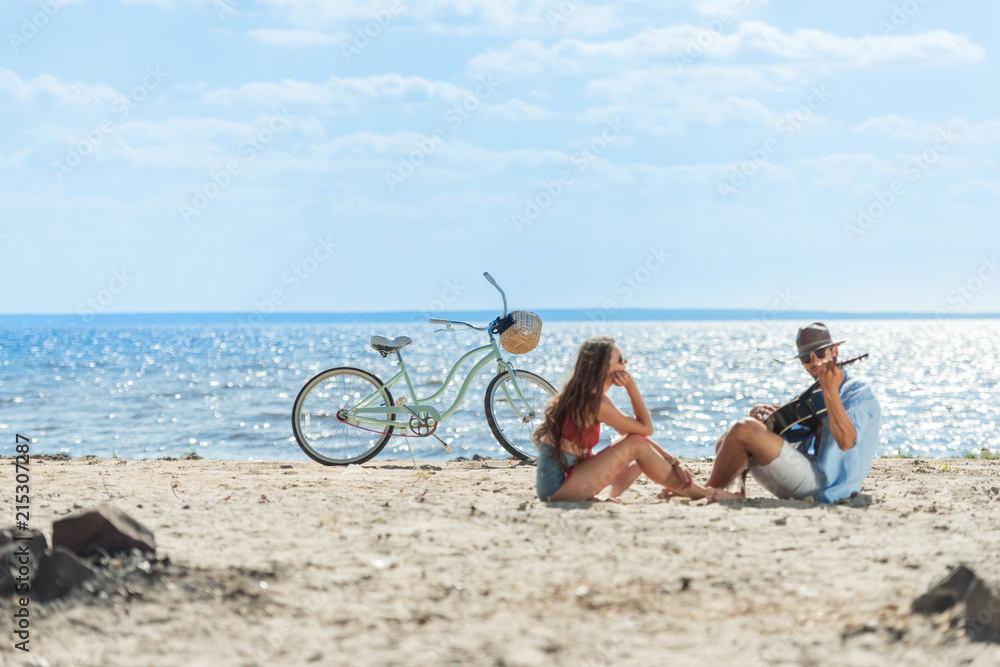 handsome man playing on guitar for his girlfriend and resting on beach with bike handsome man playing on guitar for his girlfriend and resting on beach with bike