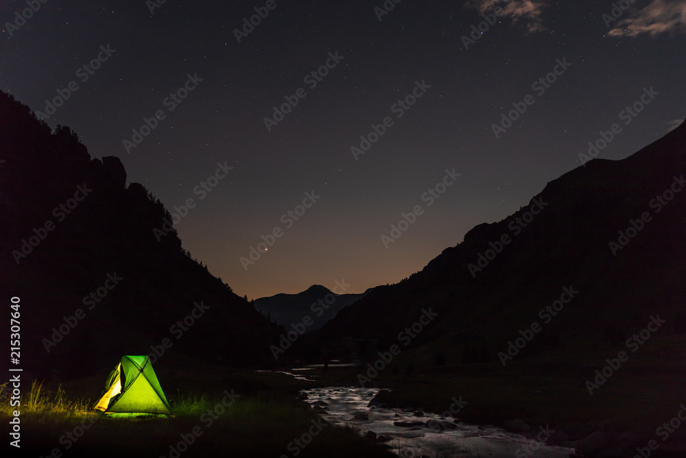 The light shines through the tent in a nocturnal mountain landscape