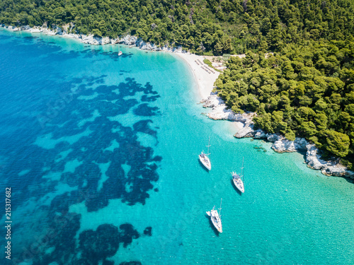 Three sailing boats anchored near the private beach on the island of Skopelos in Greece. View from above at Kastani beach