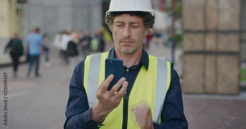 portrait mature construction engineer man using smartphone browsing working on site wearing safety helmet reflective clothing in city slow motion portrait mature construction engineer man using smartphone browsing working on site wearing safety helmet reflective clothing in city slow motion