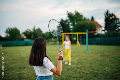 Two girls playing badminton on a green field.